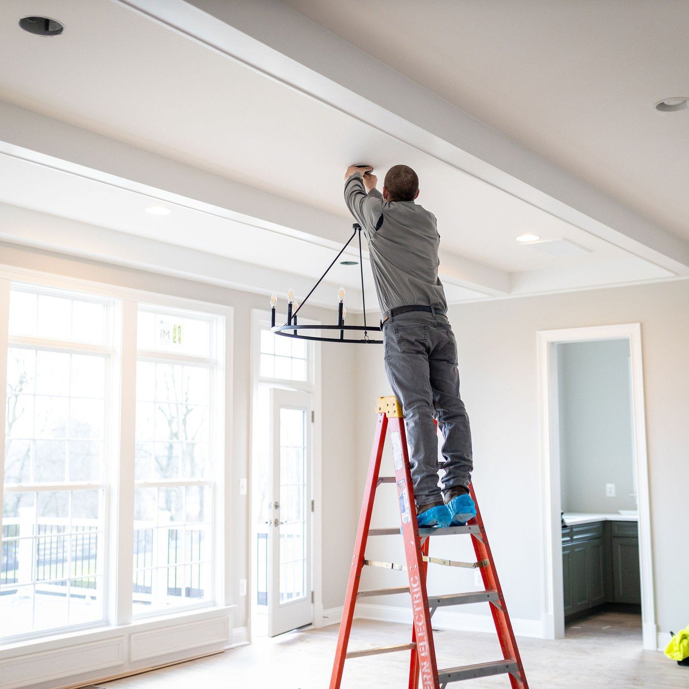 Electrician carefully installing a ceiling light fixture standing on a ladder.
