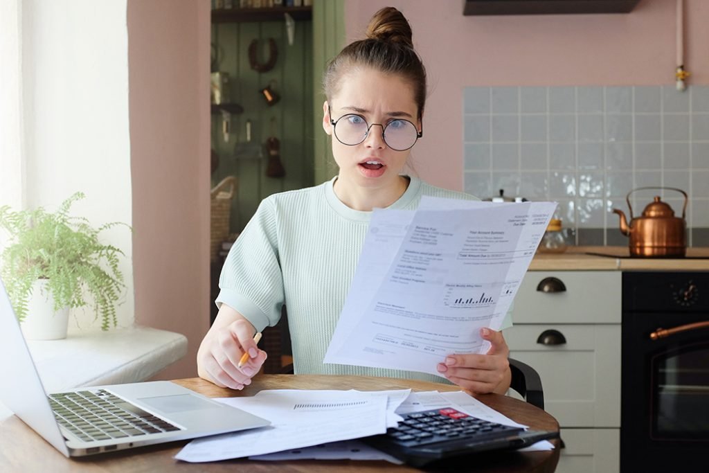 Surprised homeowner holding an electric bill with a shocked expression, reacting to unexpectedly high electricity charges.