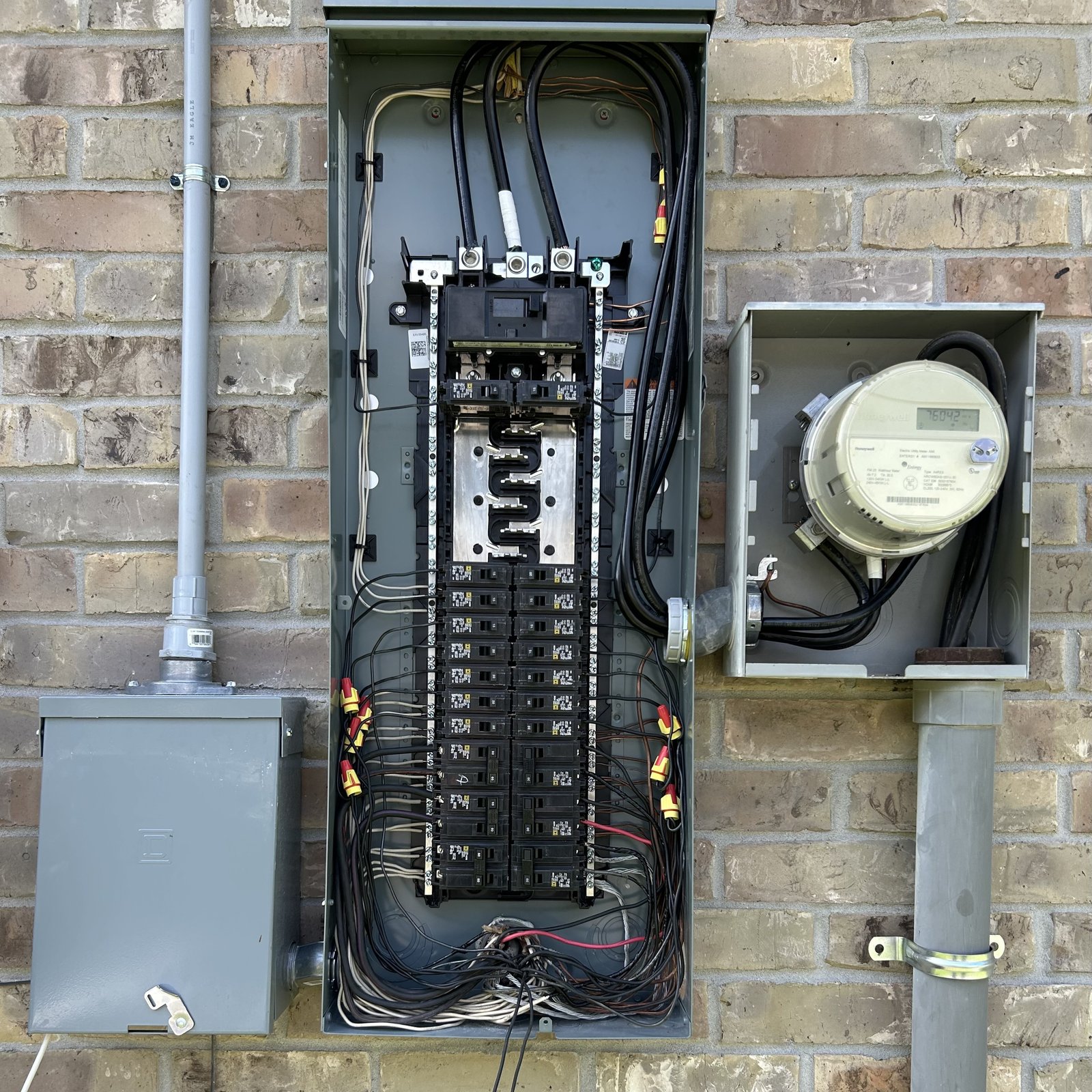 Completed exterior electrical panel upgrade beside the electric meter on a brick home